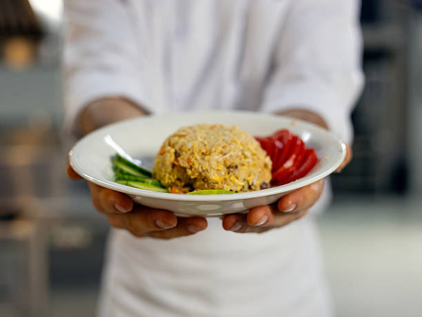 istock Close up Chef in uniform holds a plate with fried rice, garnished with fresh cucumber and tomato slices, ready to be served in restaurant 2234312965