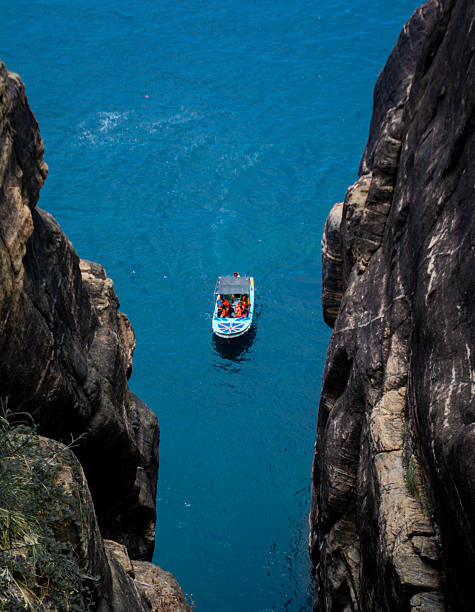 A vibrant, scenic view of the Indian Ocean from the cliffside of Koneswaram Kovil. The turquoise water and clear skies contrast beautifully with the dramatic rock formations, while small fishing or tour boats float peacefully in the bay below. This image captures the stunning natural beauty and coastal landscape of Trincomalee.