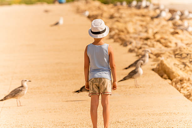 A little 3 y.o girl in a striped swimsuit running and playing on the beach with a green shovel in her hand. Image, toned in warm summer colors. Shot taken on the Baltic sea in Kaliningrad region.