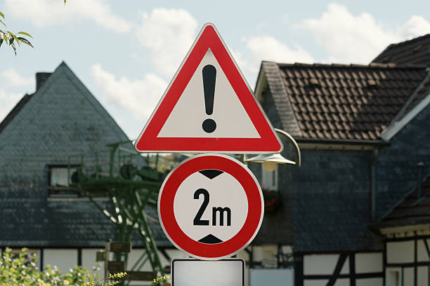 Red and white triangular give way sign indicating priority road in residential area with blurred background of brick buildings and parked car