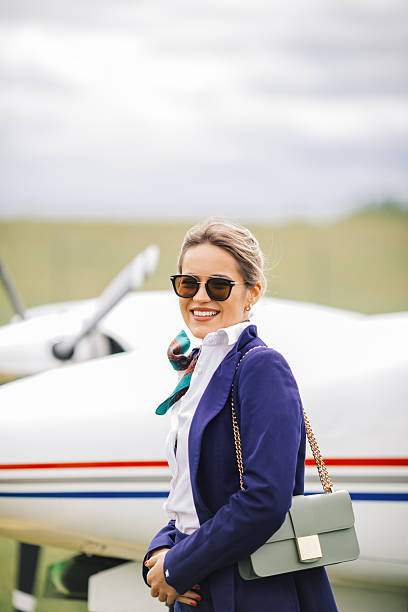 Young successful girl getting out of a private jet parked on a runway.  She is holding onto the railing of the boarding stairs.