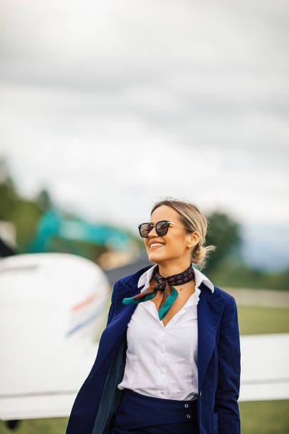 Young blond woman, stewardess standing in front of an airplane, smiling, getting ready for a flight.