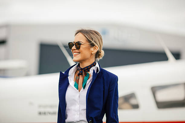 Young blond woman, stewardess standing in front of an airplane, smiling, getting ready for a flight.