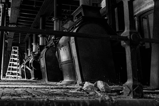 Vintage machinery stands in disuse within a deserted workshop, surrounded by dust and old wooden structures.
