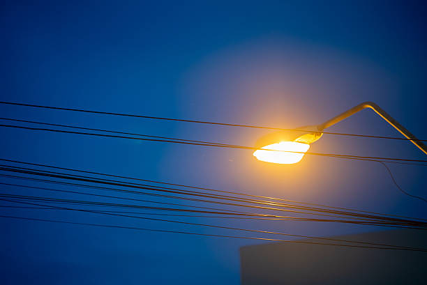 A close-up view of a glowing street lamp against a rich blue evening sky, capturing the ambiance of urban life with illuminated wires and peaceful atmosphere.