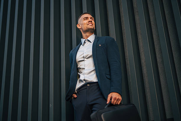 Businessman looking up with briefcase in hand, leaning against modern building