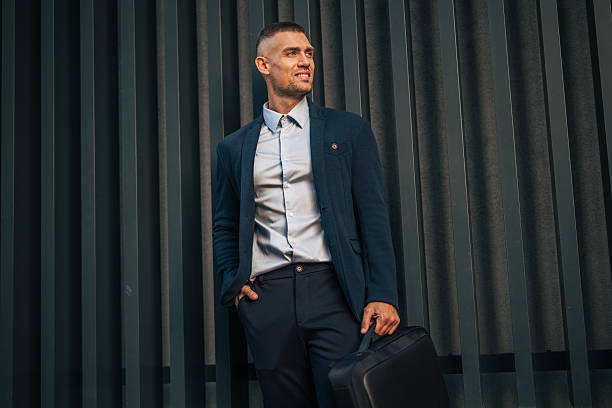 istock Businessman leaning against wall holding briefcase smiling 2234324633