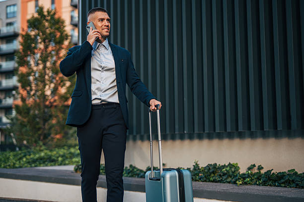 istock Businessman walking with luggage and talking on phone near modern building 2234324708