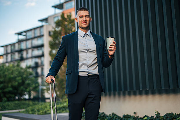 istock Smiling businessman walking with suitcase and coffee in urban setting 2234324713