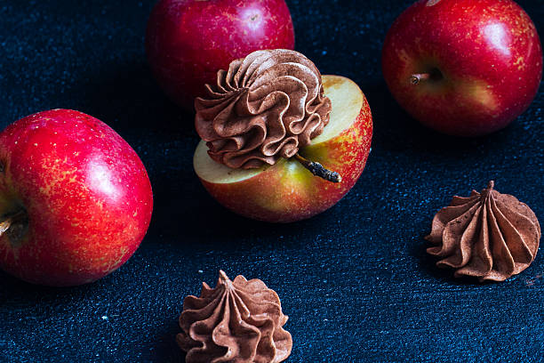Red apples are beautifully presented with a chocolate cream topping, creating an enticing dessert scene with whole apples scattered on a dark textured background