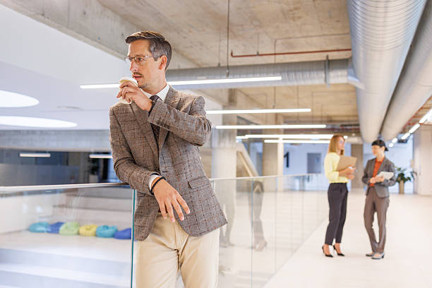 istock Businessman drinking coffee and looking away while coworkers chatting in background 2234338246