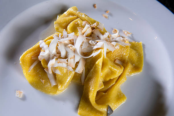A professional chef carefully shapes fresh, handmade tortellini on a floured wooden board, highlighting the traditional Italian culinary art. The image captures the meticulous process and skill required to create this iconic pasta, showcasing an authentic, rustic food preparation scene.