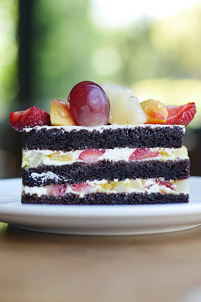 A slice of chocolate cake with layers of cream and fresh fruits on top.