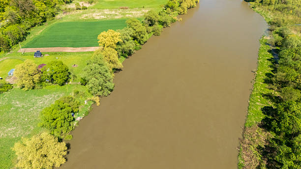 istock Aerial view of a serene river landscape featuring lush greenery, a brown river, and open fields. The scene captures tranquil nature in springtime, ideal for environmental themes. 2234354976