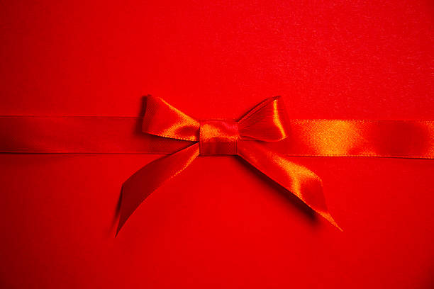 Red satin ribbon with bow on red background, top view