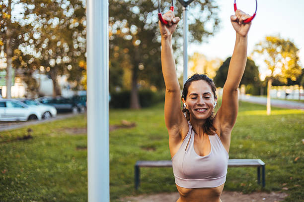 A woman engages in fitness activities using outdoor equipment in a scenic park, enjoying nature and sunlight. The image captures a sense of health, happiness, and an active lifestyle in an urban environment.