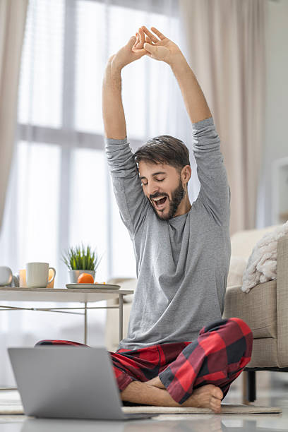 istock Young man enjoying a relaxed morning routine while stretching and working on his laptop at home 2234367452