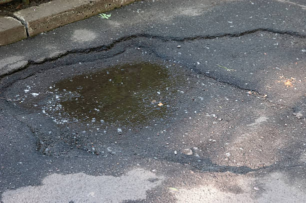 istock A small pothole in asphalt with a puddle at the bottom, surrounded and covered with poplar fluff. 2234367712