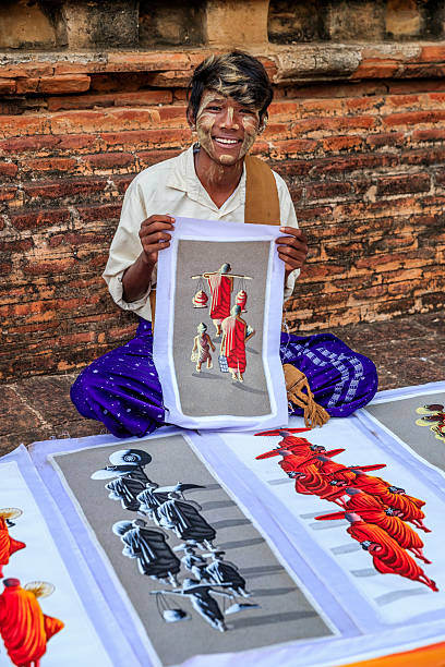 Young Burmese boy with thanaka face paint selling souvenirs - sand paintings, in the ancient temple of Bagan, Myanmar (Burma)