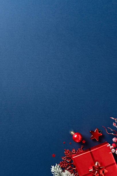 istock Festive corner composition with red gift, frosted pine branches, berries, and ornaments on dark blue background. Stylish Christmas flat lay 2234370272