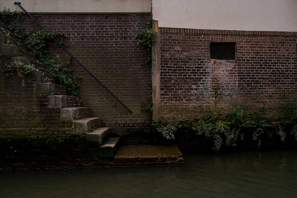 Old Dutch brick walls line a narrow canal, damp and weathered from years of exposure, creating a dingy, wet atmosphere that reflects historic charm and moody urban character.