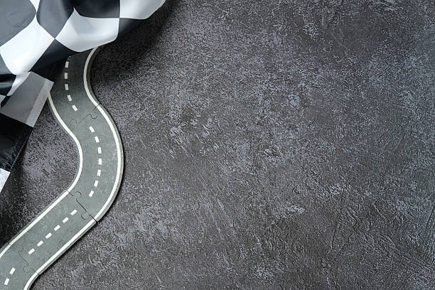 istock Curved toy road with white dashed lines on dark textured surface, checkered flag draped in corner, symbolizing racing, finish line, or playful competition concept. 2234371887
