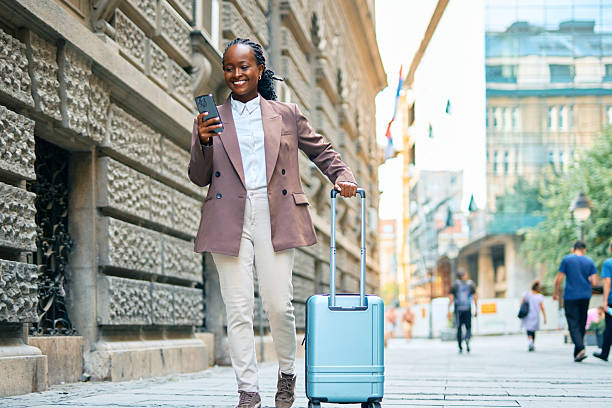 istock Young businesswoman walking down the street pulling a suitcase and using a smartphone 2234377721
