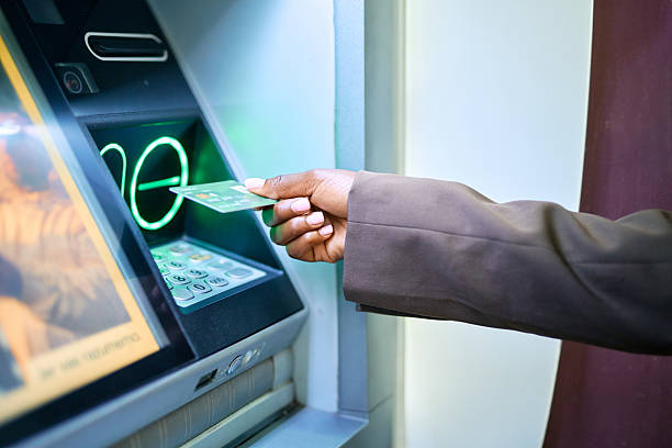 Businesswoman inserting her credit card into an ATM at night, withdrawing cash from the illuminated machine. Modern technology providing convenient access to funds for financial transactions