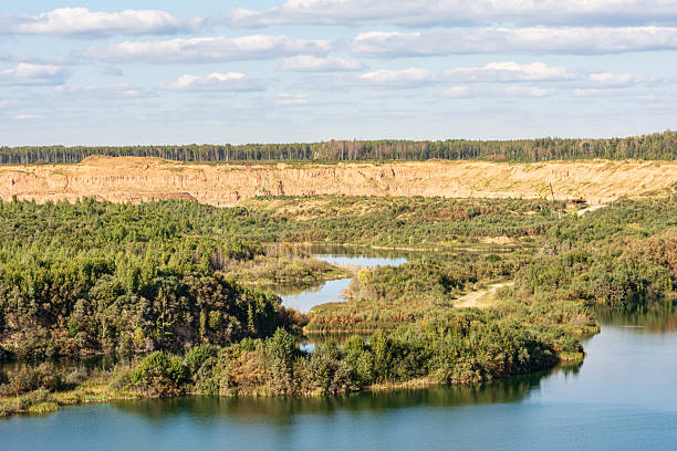 A serene landscape featuring a winding river surrounded by dense green vegetation and a sandy cliff in the background under a partly cloudy sky.