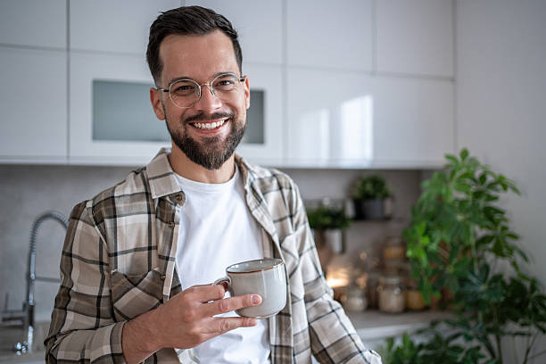 istock Smiling young man enjoying a cup of coffee in his modern kitchen 2234383333