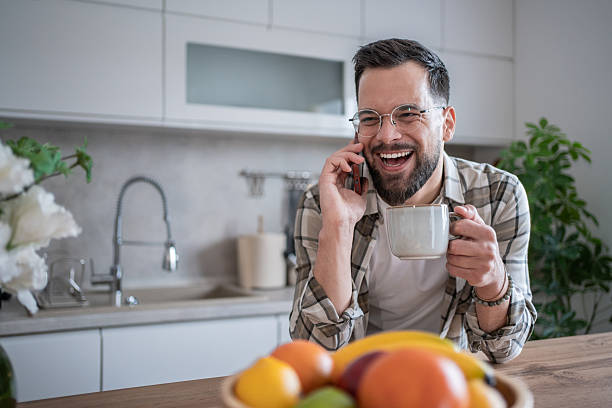 istock Happy man laughing while talking on phone and drinking coffee in kitchen 2234383475