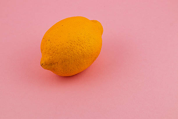 Bright yellow lemon resting on pink background highlighting its texture
