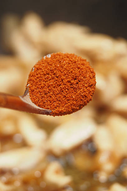 A close-up of red spice on a spoon above sliced ingredients in a pan.