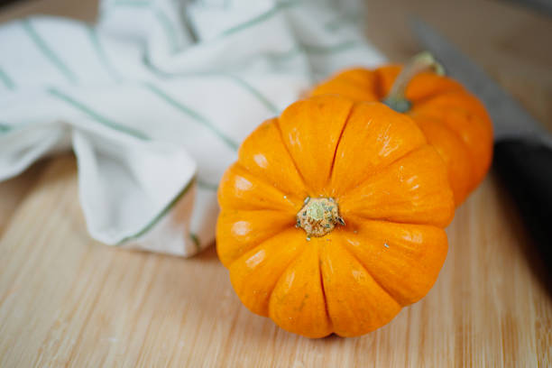 Vibrant orange pumpkins sit on a wooden surface near a knife.
