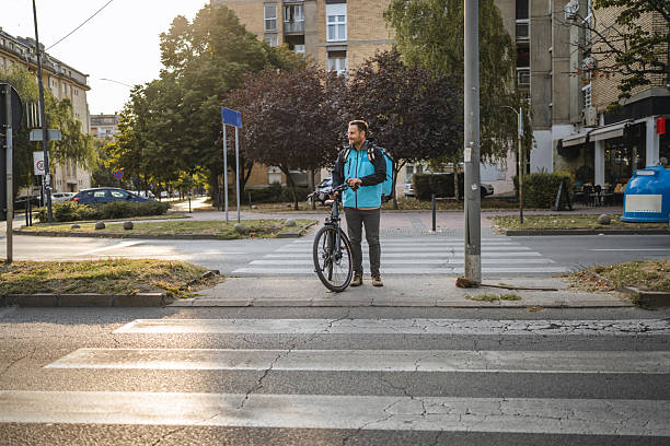 istock Delivery man waiting at crosswalk with bicycle during delivery round 2234386175
