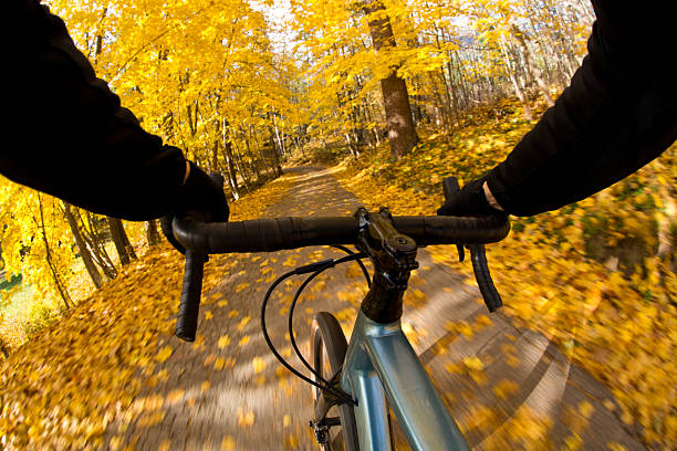 The handlebar view of an autumn road bike ride near Nelson, British Columbia, Canada. The cyclist is riding a gravel road bike on a quiet country road. Gravel bikes are like road bicycles but have sturdy wheels and tires for riding on rough terrain.