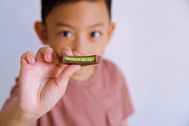 Close up portrait of young boy holding chocolate bar towards camera, showing detail of hand and sweet snack.