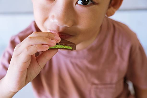 Close up of young boy eating chocolate bar, showing detail of child’s mouth and hand holding sweet snack.