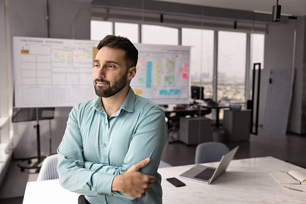 Thoughtful professional man stands with arms crossed in modern office