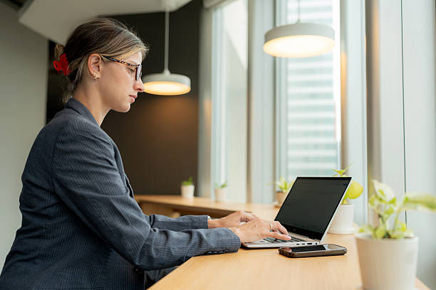 istock An office employee is working on a computer at a counter bar in a modern workplace, seated by a large window overlooking tall skyscrapers. The scene reflects focus, teamwork, and a corporate culture that values communication 2234406089