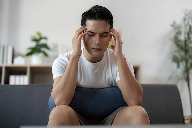 Mental Health. Young man experiencing headache while sitting on couch at home.