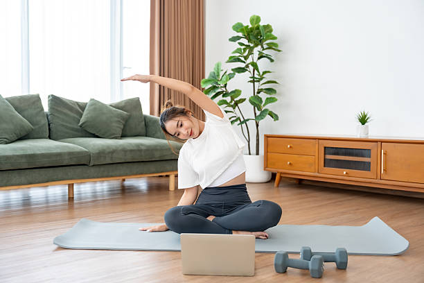 istock Young Asian woman stretching yoga workout on exercise mat while online training class with computer laptop in living room 2234414915