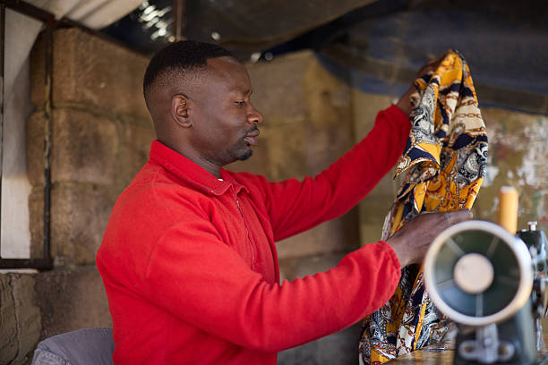 Tailor examining fabric while sitting at shop. Man picking up piece of cloth at tailor shop. He is wearing red jacket.
