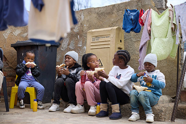 Group of children eating sandwiches while sitting together on steps. Siblings are talking with each other while having meal. Concept of togetherness and friendship.
