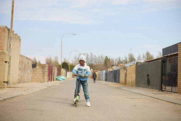 Full length of boy riding push scooter in middle of road against sky. Boy is playing outdoors on weekend. He is wearing casuals.