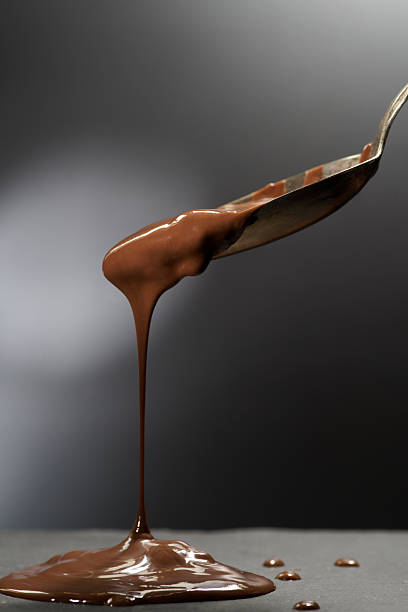 istock Sweet liquid chocolate flows from a tilted metal spoon against a dark background 2234424383
