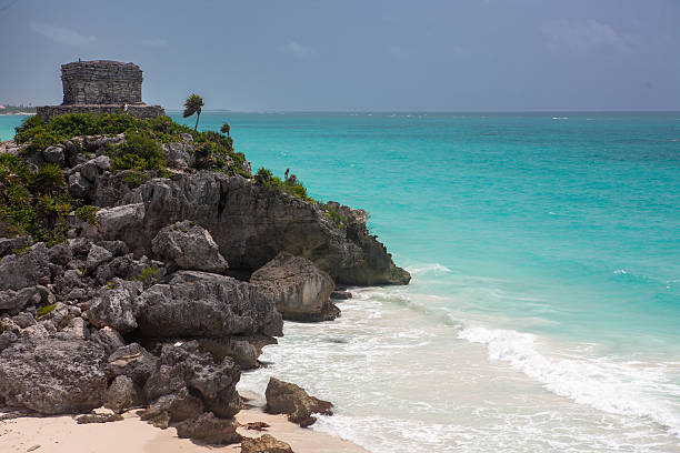 The iconic Mayan temple of Tulum standing on a cliff above a white sandy beach and turquoise waters of the Caribbean Sea.