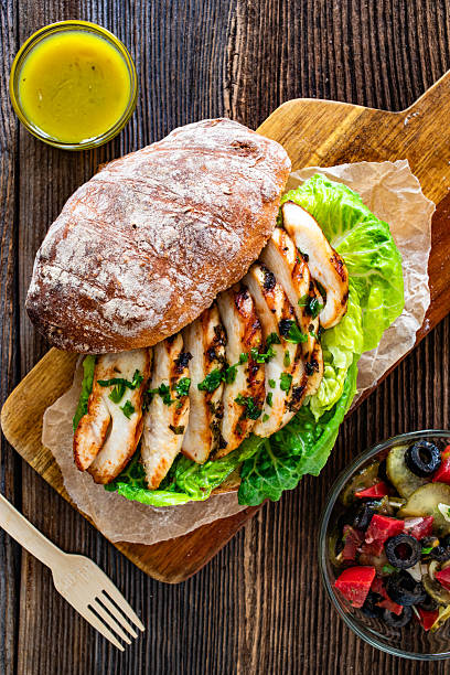 Takeaway sandwich with slices of grilled chicke breast on wooden table