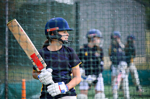 istock Girls lined up in nets practicing batting wearing protective sports helmets and padding holding cricket bats 2234429220