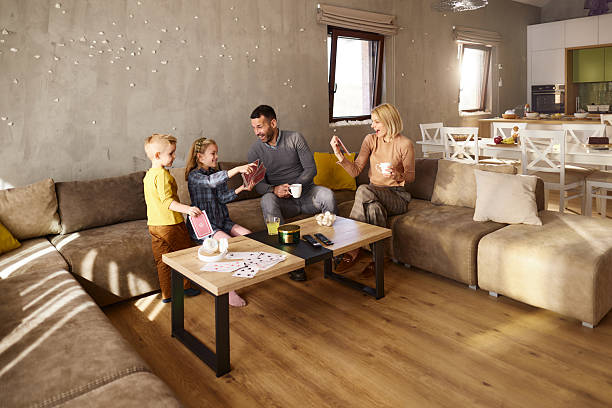 Happy parents enjoying in coffee while relaxing with their kids who are playing with cards on sofa in the living room.